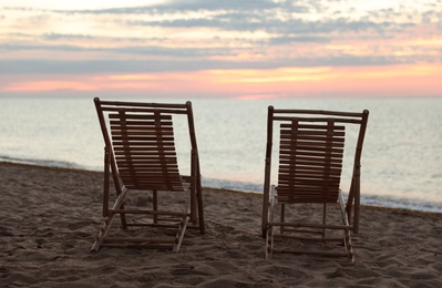 Photo of Wooden deck chairs on sandy beach at sunset. Summer vacation