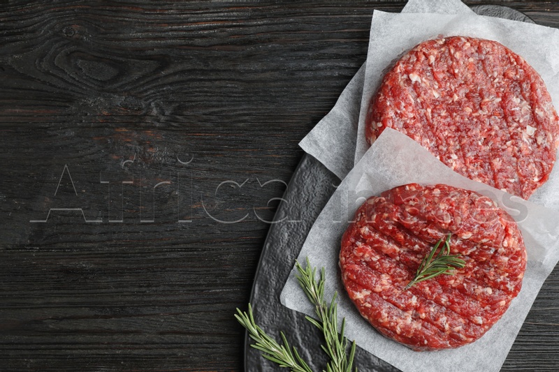 Raw meat cutlets for burger on black wooden table, top view. Space for text
