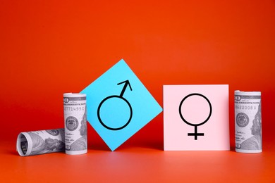 Photo of Gender pay gap. Male and female symbols near dollar banknotes on red background