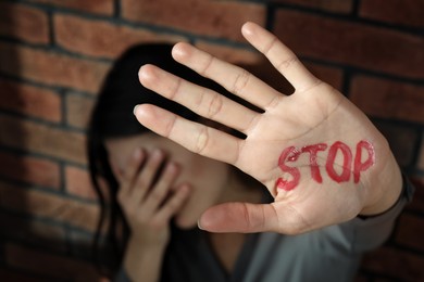 Photo of Domestic violence concept. Unhappy woman near brick wall, focus on hand with written word Stop