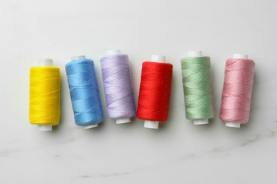 Photo of Colorful sewing threads on white marble table, flat lay