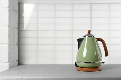 Stylish electric kettle on grey table against white wall, space for text. Tea preparation