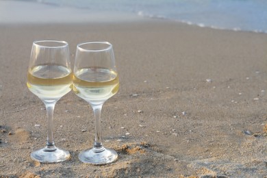 Photo of Glasses of tasty wine on sandy beach, space for text