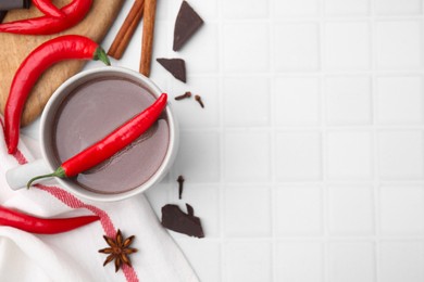 Photo of Cup of hot chocolate with chili pepper on white tiled table, flat lay. Space for text