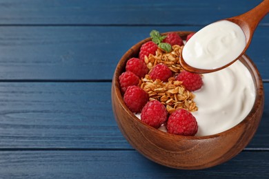Eating tasty yogurt with raspberries and muesli from bowl on blue wooden table. Space for text