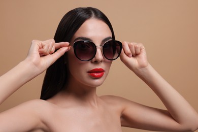 Attractive woman wearing fashionable sunglasses against beige background