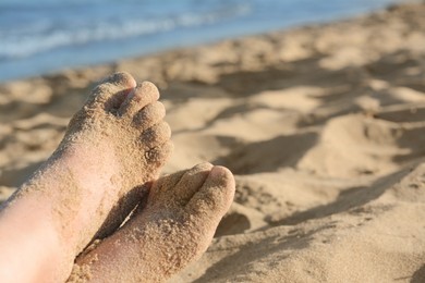 Photo of Child resting on sand near sea, closeup of feet. Space for text