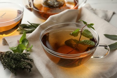 Photo of Cup of aromatic herbal tea with rosemary, sage, thyme and mint on table