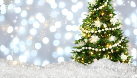 Snow and beautiful decorated Christmas tree against blurred festive lights, bokeh effect. Space for text