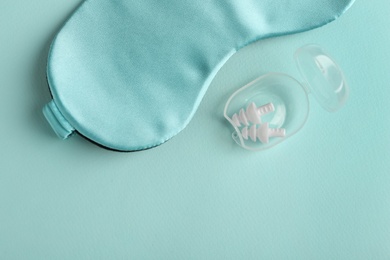 Pair of ear plugs in case and sleeping mask on turquoise background, flat lay