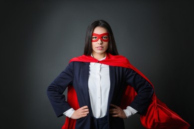 Confident businesswoman wearing superhero cape and mask on grey background