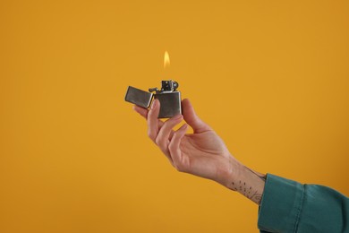 Woman holding lighter with burning flame on orange background, closeup