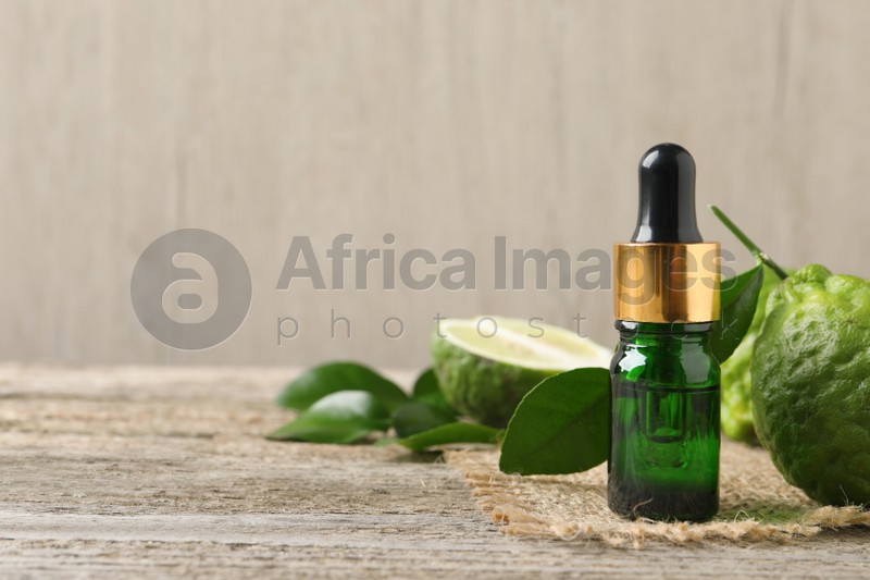 Photo of Bottle of essential oil and fresh bergamot fruits on wooden table. Space for text