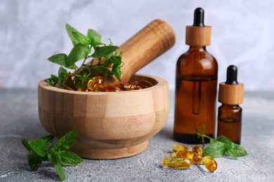 Wooden mortar with fresh green herbs, extracts and capsules on light grey table