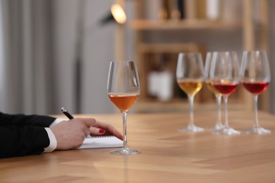 Sommelier making notes during wine tasting at table indoors, closeup
