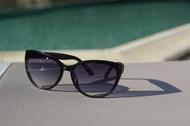 Stylish sunglasses near outdoor swimming pool on sunny day, space for text