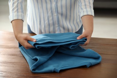 Woman folding clothes at wooden table indoors, closeup