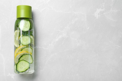 Bottle of refreshing water with cucumber, lemon and mint on light grey table, top view. Space for text