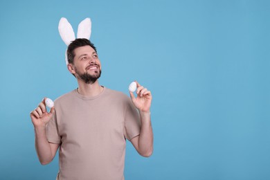 Photo of Happy man in bunny ears headband holding painted Easter eggs on turquoise background. Space for text