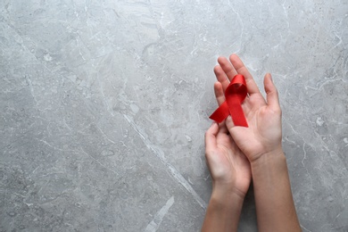 Woman holding red awareness ribbon at light grey marble table, top view with space for text. World AIDS disease day