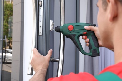 Handyman with screw gun repairing door lock outdoors, closeup