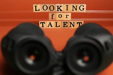 Photo of Staff recruitment concept. Phrase Looking For Talent made of wooden cubes and binoculars on orange background, selective focus