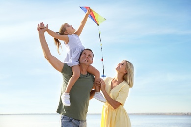 Happy parents with their child playing with kite on beach. Spending time in nature