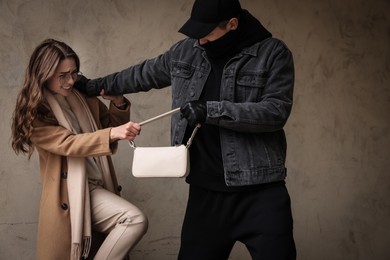 Woman fighting with thief while he trying to steal her bag near beige wall. Self defense concept