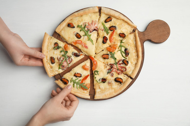 Women taking pieces of delicious seafood pizza at white wooden table, top view
