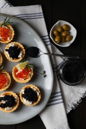Photo of Delicious tartlets with red and black caviar served on dark table, flat lay