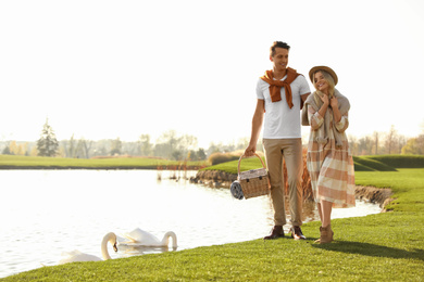 Young couple with picnic basket near lake on sunny day