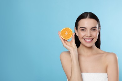 Photo of Woman holding half of orange on light blue background, space for text. Spa treatment