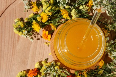 Delicious fresh honey in glass jar and beautiful flowers on wooden table, flat lay