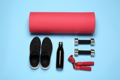 Exercise mat, dumbbells, bottle of water, skipping rope and shoes on light blue background, flat lay