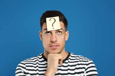 Pensive man with question mark sticker on forehead against blue background