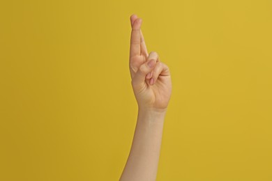 Woman showing crossed fingers on yellow background, closeup