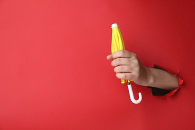 Woman holding closed small yellow umbrella through hole in red paper, closeup. Space for text