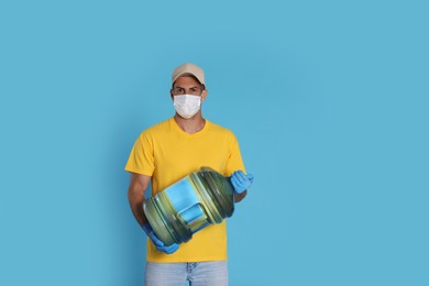 Courier in medical mask holding bottle for water cooler on light blue background. Delivery during coronavirus quarantine
