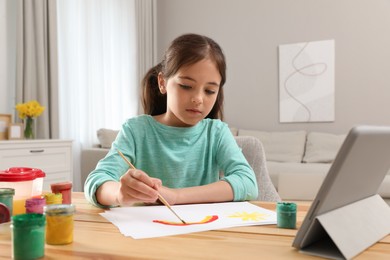 Little girl drawing on paper with paints at online lesson indoors. Distance learning