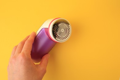Photo of Woman holding modern fabric shaver on yellow background, closeup. Space for text
