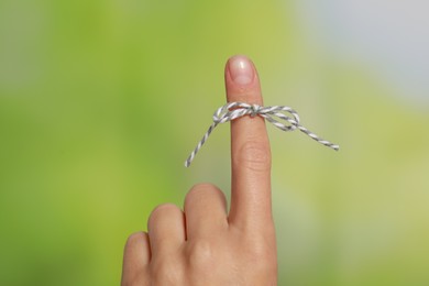 Photo of Woman showing index finger with tied bow as reminder on green blurred background, closeup