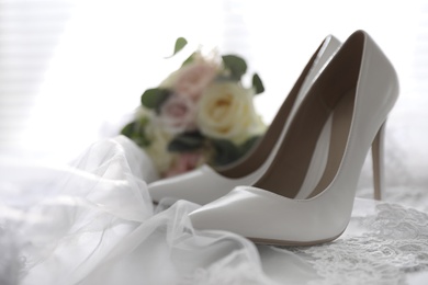 Pair of white high heel shoes, veil and wedding bouquet on light background