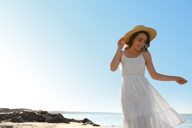 Happy young woman with hat on beach near sea. Space for text