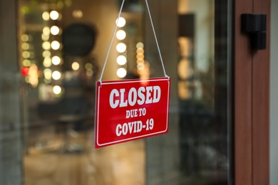 Red sign with words Closed Due To Covid-19 hanging on glass door, closeup