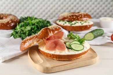 Delicious bagel with cream cheese, jamon, cucumber and parsley on white wooden table
