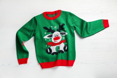 Photo of Warm Christmas sweater on white wooden table, top view