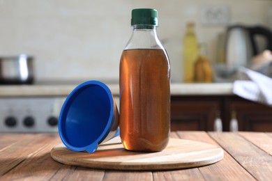 Bottle with used cooking oil and funnel on wooden table in kitchen