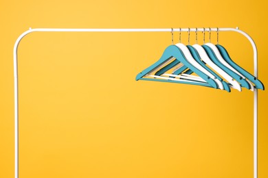 Photo of Bright clothes hangers on metal rack against yellow background