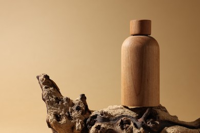 Photo of Wooden bottle of cosmetic product on tree bark against dark beige background, space for text