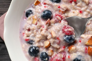 Photo of Tasty oatmeal porridge with toppings on wooden table, top view